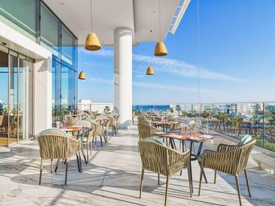 Moderne Dachterrasse mit Tischen, Stühlen und Blick auf Stadt und Meer bei klarem Himmel.