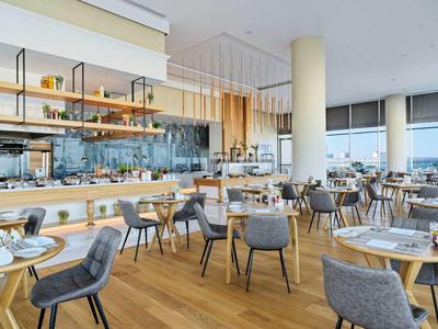 Modern restaurant with wooden floor, grey chairs, and large windows overlooking the city.