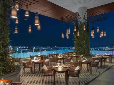 Luxuriöse Terrasse mit Holztischen, Korbstühlen und Laternen über der Stadt bei Nacht.