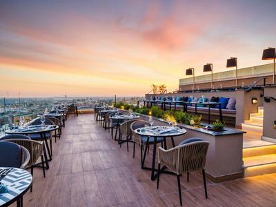 Terrace with tables and chairs, overlooking the city at sunset.