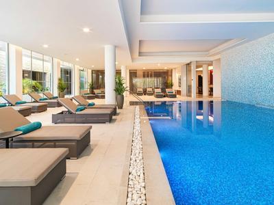 Moderner Innenpool mit blauen Fliesen, bequemen Liegen und großen Fenstern für viel Tageslicht.