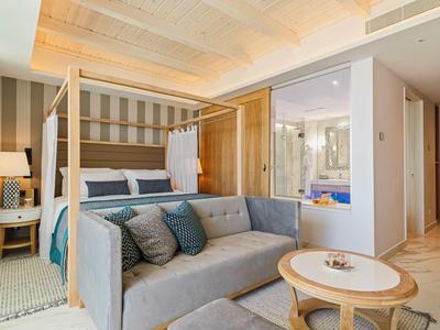 Helles Schlafzimmer mit Himmelbett, grauem Sofa und kleinem runden Tisch in modernem Stil.