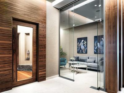 Moderner Wohnbereich mit Glaswand, grauem Sofa, blauen Sesseln und Holzrahmen an der Tür.