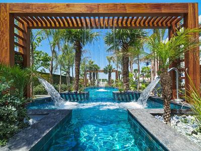 Pool with waterfalls and wooden pergola surrounded by palm trees in tropical hotel setting