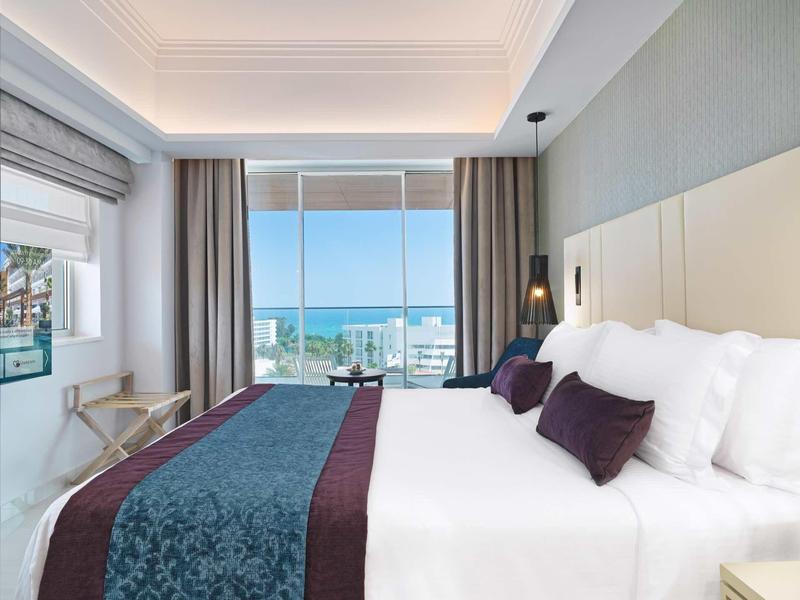 Modernes Hotelzimmer mit großem Bett, Meerblick, hellen Wänden und stilvoller Dekoration.