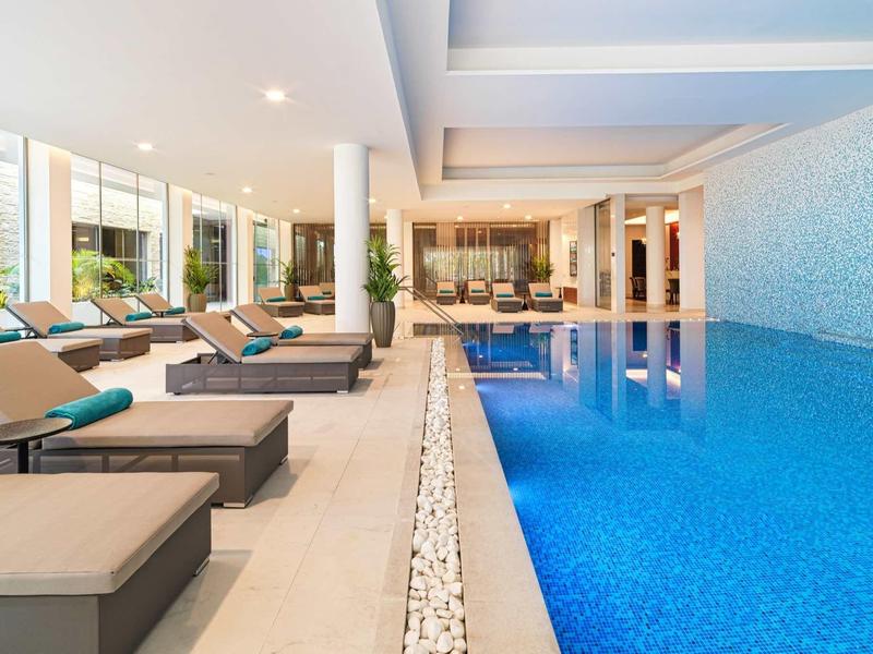 Moderner Innenpool mit blauen Fliesen, bequemen Liegen und großen Fenstern für viel Tageslicht.