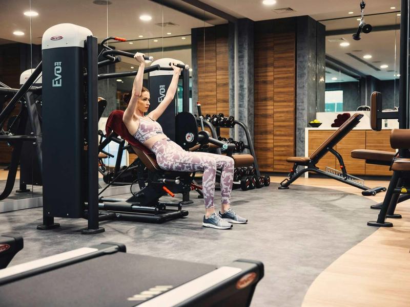 Frau trainiert an Kraftmaschine in modern ausgestatteter Fitnessstudio-Umgebung mit Holzwand.