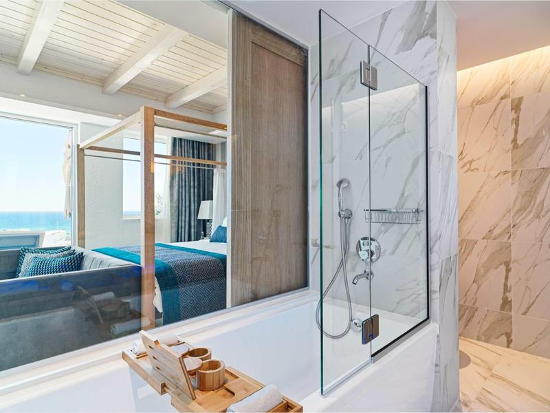 Modernes Badezimmer mit Glas-Dusche, weißen Marmorwänden und großem Fenster zum Schlafzimmer.