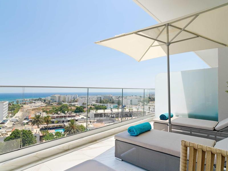 Terrassenblick aufs Meer mit moderner Lounge, weißem Sonnenschirm und klarem Himmel.