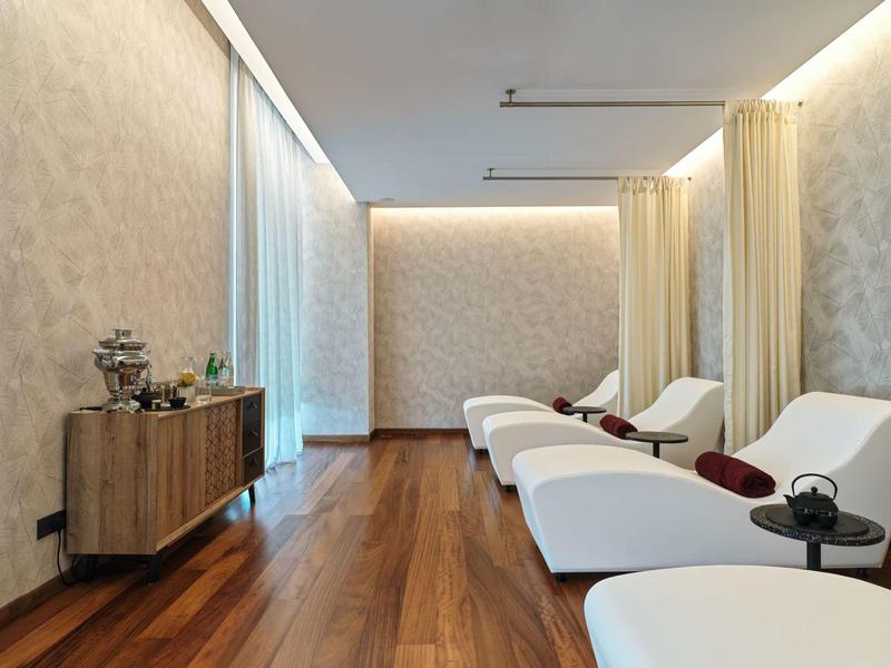 Moderner Ruheraum mit weißen Liegesesseln, Holzboden, sanftem Licht und einer Kommode an der Wand.