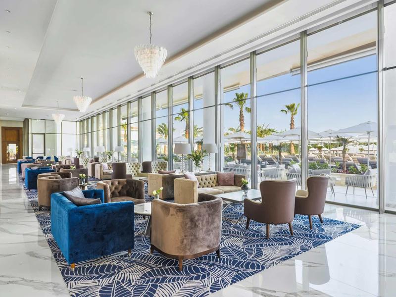 Moderne Lounge mit großen Fenstern, blauen und braunen Sesseln auf blau gemustertem Teppich.