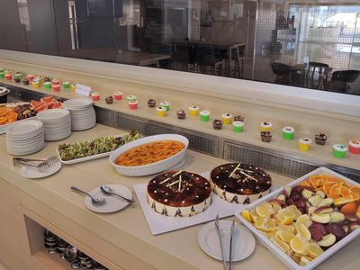 Buffet mit Kuchen, Obst, Salaten und verschiedenen kleinen Desserts in Gläsern auf weißem Tisch.
