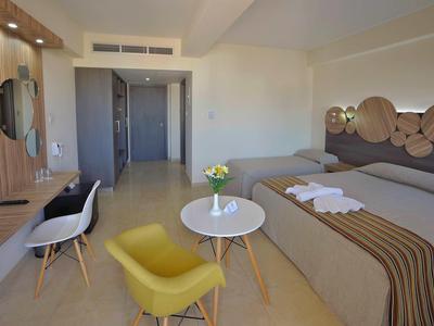 Modernes Hotelzimmer mit zwei Betten, Sitzbereich, Fernseher und hellem, freundlichem Interieur.