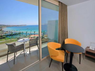 Moderner Raum mit zwei orangen Sesseln, Rundtisch und Blick auf Balkon mit Meer und Strand.