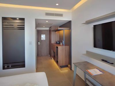 Modernes Hotelzimmer mit Fernseher, Holzmöbeln, indirekter Beleuchtung und hellen Wänden.