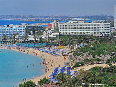 Strand mit blauem Meer, Sonnenschirmen, Palmen und großen Hotels im Hintergrund unter klarem Himmel.