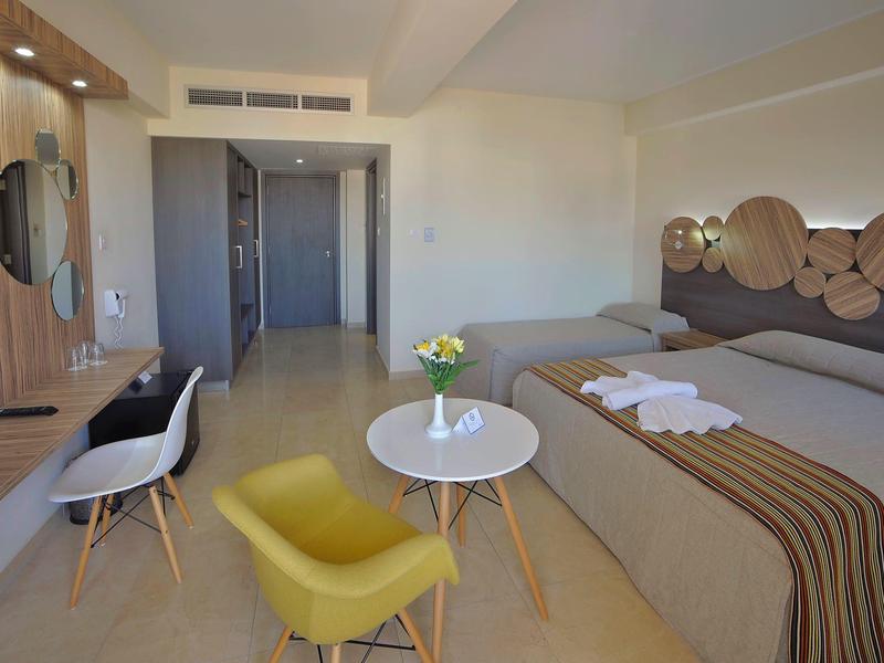 Moderní hotelový pokoj se dvěma postelemi, stolem, židlemi a televizí na stěně.