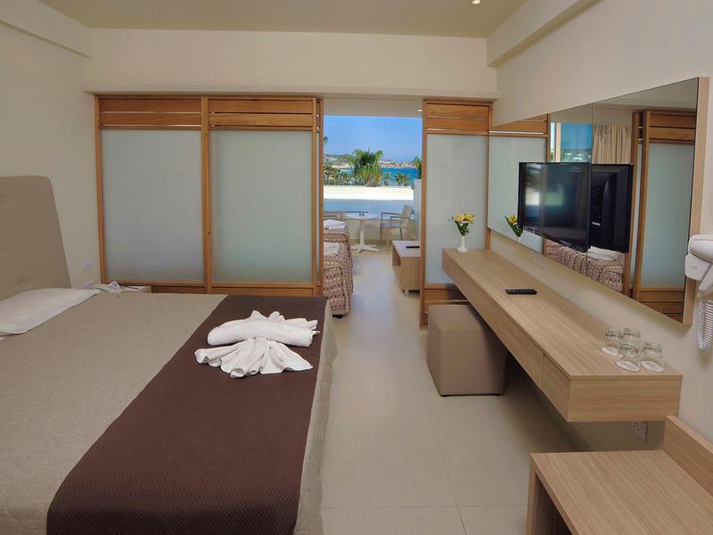 Moderní hotelový pokoj s velkou postelí, stolem a výhledem na terasu s bazénem