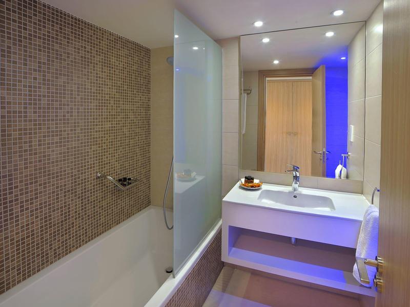 Moderní koupelna s vanou, skleněnou přepážkou a velkým zrcadlem s umyvadlem.