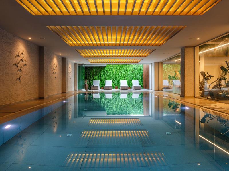 Vnitřní bazén s moderními lehátky a zelenou stěnou v pozadí