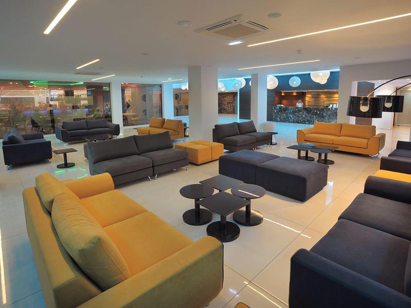 Moderní hotelová lounge s jasnými pohovkami a malými stolky na lesklé podlaze.