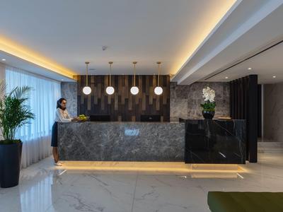 Reception moderna di un hotel con bancone in marmo, personale e illuminazione raffinata.