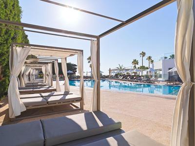 Poolbereich mit blauer Wasserfläche, weißen Liegen und Holzbettgestellen mit weißen Vorhängen.