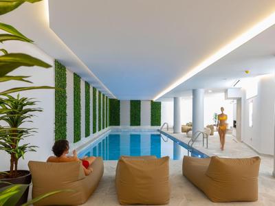 Zona piscina interna con pouf, piante verdi a parete e luce naturale.