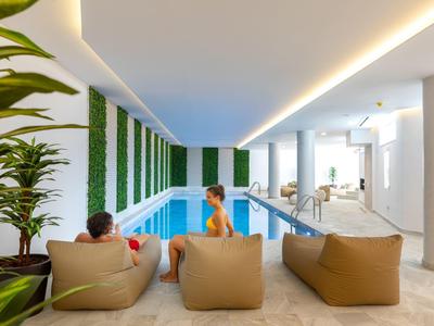 Moderner Indoor-Pool mit grünen Wandpaneelen, bequemen Sitzsäcken und zwei Menschen im Wasser.