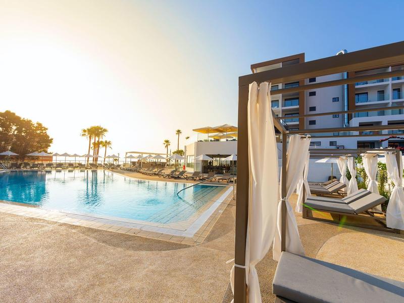 Moderner Poolbereich bei Sonnenuntergang mit Liegen, Sonnenschirmen und angrenzendem Hotelgebäude.