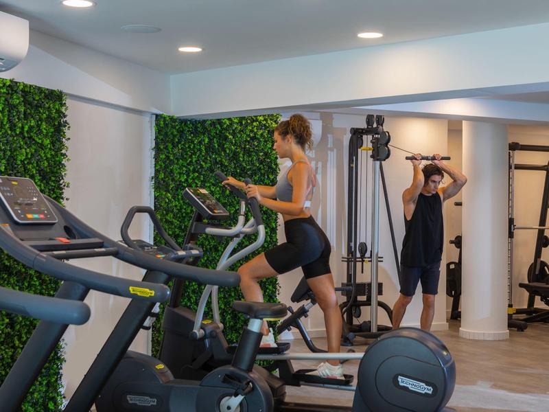 Frau trainiert auf dem Laufband, Mann nutzt Kabelzuggerät, moderner Fitnessraum mit grünen Wandakzenten.