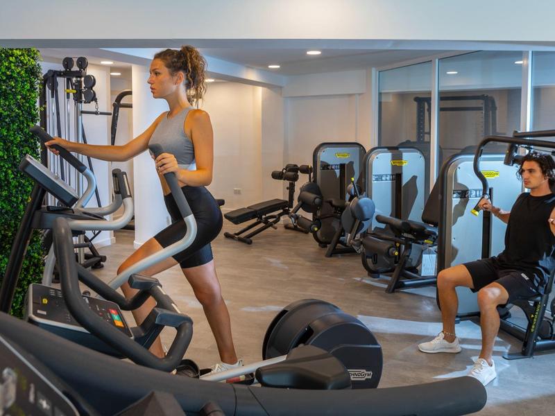 Frau trainiert auf Crosstrainer, Mann nutzt Kraftmaschine im gut ausgestatteten Fitnessraum.