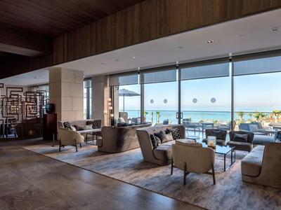 Elegante área de lounge del hotel con zonas de descanso y grandes ventanas con vista al mar.
