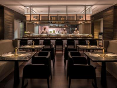 Elegantes Restaurant mit dunklen Holztischen, schwarzen Sesseln und gedämpfter Beleuchtung.