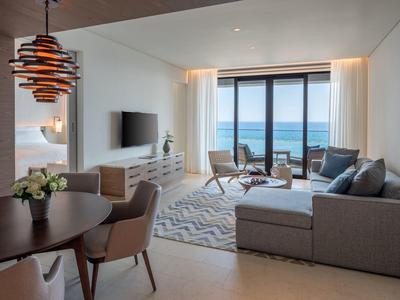 Helles Wohnzimmer mit grauem Sofa, runden Tisch, Stühlen, Holzlampe und Meerblick durch große Fenster.