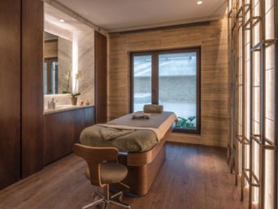 Gemütlicher Massageraum mit Holzwänden, weichem Licht und einem großen Fensterblick.