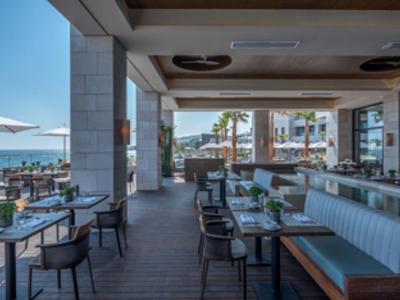 Moderner, offener Restaurantbereich mit Tischen, Stühlen, Baumdekoration und Blick aufs Meer.