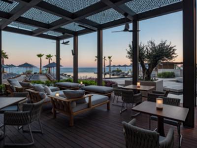Terrasse mit Holzboden, gemütlichen Sitzgruppen und Blick auf Meer und Palmen bei Sonnenuntergang.