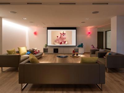 Moderner Wohnraum mit drei Sofas, großem Fernseher und warmem, indirektem Licht.