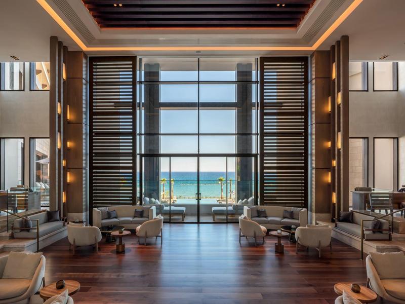 Großer, heller Raum mit Holzboden, Sesseln und Panoramafenster mit Blick aufs Meer.