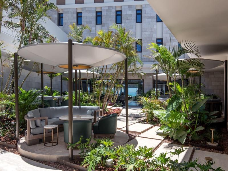 Moderner Außenbereich mit runden Tischen, Stühlen, Sonnenschirmen und vielen grünen Pflanzen.