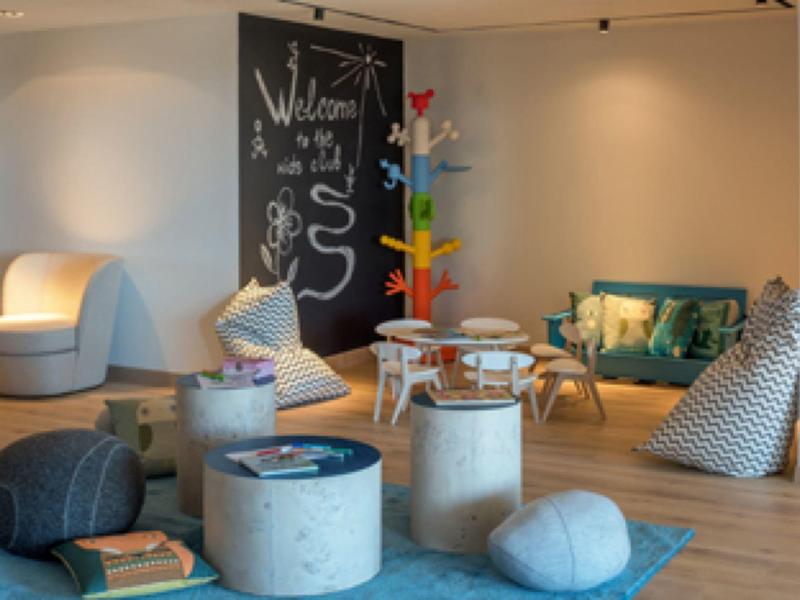 Gemütliches Wohnzimmer mit bunten Sitzkissen, Sessel, Sofa, buntem Baum und Holztisch auf blauem Teppich.