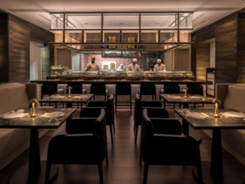 Elegantes Restaurant mit dunklen Holztischen, schwarzen Sesseln und gedämpfter Beleuchtung.