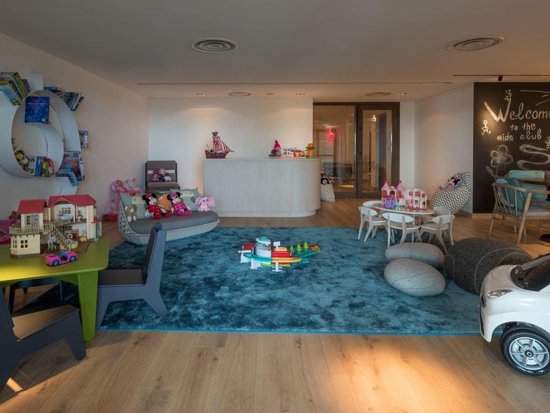 Kinderspielecke mit buntem Teppich, Spielzeugautos, Tischen, Stühlen und bunter Dekoration.