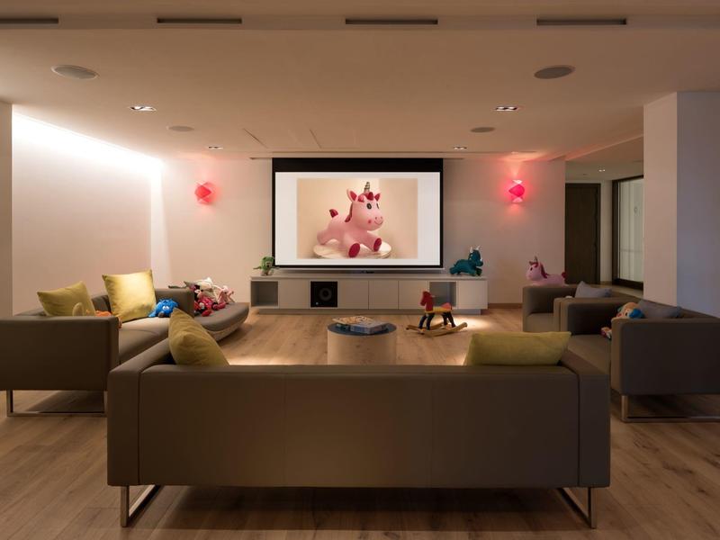 Moderner Wohnraum mit drei Sofas, großem Fernseher und warmem, indirektem Licht.