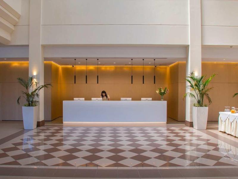 Světlá hotelová recepce s moderním pultem a velkými kvetináči.