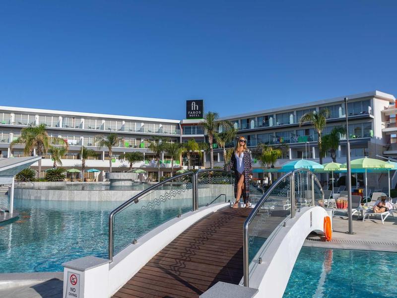 Moderní hotelový komplex s bazénem, mostem a palmami pod jasnou oblohou.