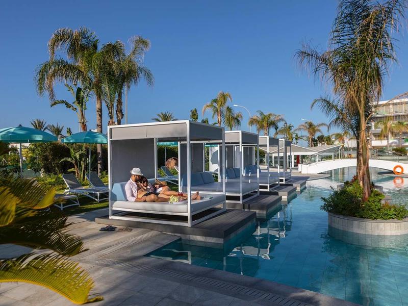 Luxusní lehátka u hotelového bazénu s deštníky a palmami za slunečného dne.