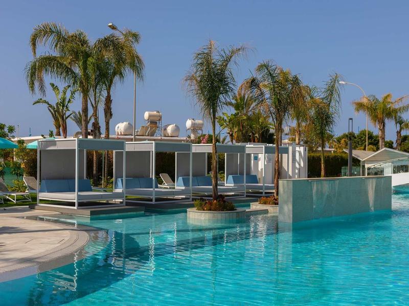 Moderní hotelový bazén s lehátky a palmami pod jasnou oblohou