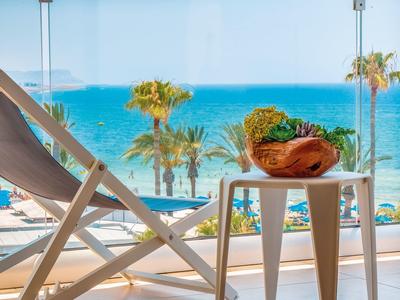 A deck chair and small table with fruit in front of a glass wall overlooking palm trees and the sea.